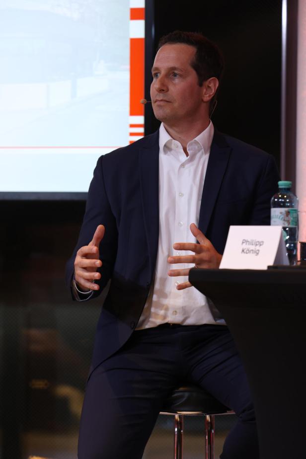 Ein Mann im Anzug spricht auf einer Podiumsdiskussion, vor ihm steht ein Namensschild.