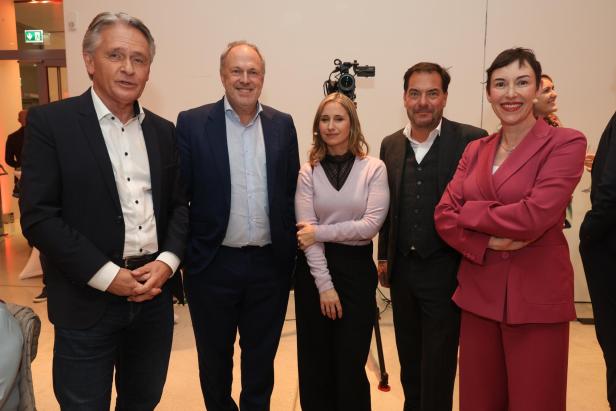 Fünf Personen stehen nebeneinander und lächeln in die Kamera, im Hintergrund eine Kamera auf Stativ.