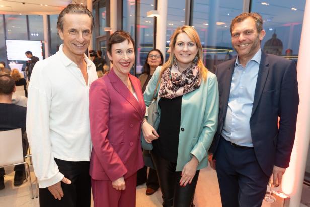 Vier Personen stehen lächelnd nebeneinander bei einer Veranstaltung im Innenraum.