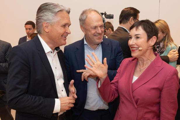 Drei Personen im Gespräch, eine Frau trägt ein Headset-Mikrofon und lächelt.