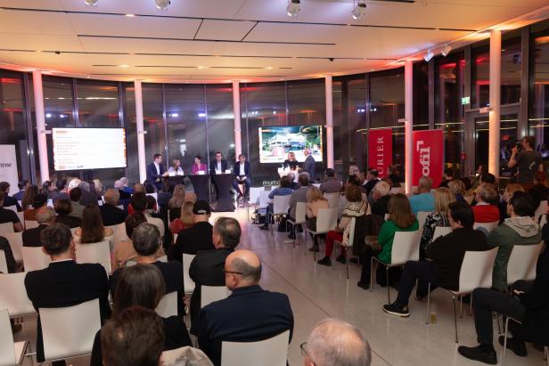 Podiumsdiskussion mit Publikum in einem modernen, hell erleuchteten Veranstaltungsraum.
