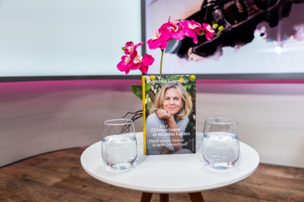 Auf einem Tisch stehen das Buch "Der Zitronenbaum in meinem Garten" von Andrea L'Arronge, zwei Gläser Wasser und eine Orchidee.