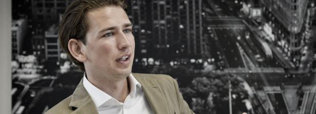 Ein Mann in einem hellbraunen Sakko vor einem Schwarz-Weiß-Foto einer Stadt.