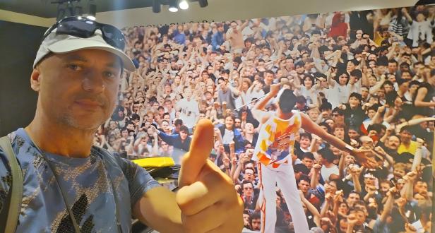 Edwin Schmidt posiert vor einem großen Bild von Freddie Mercury und einer jubelnden Menschenmenge.