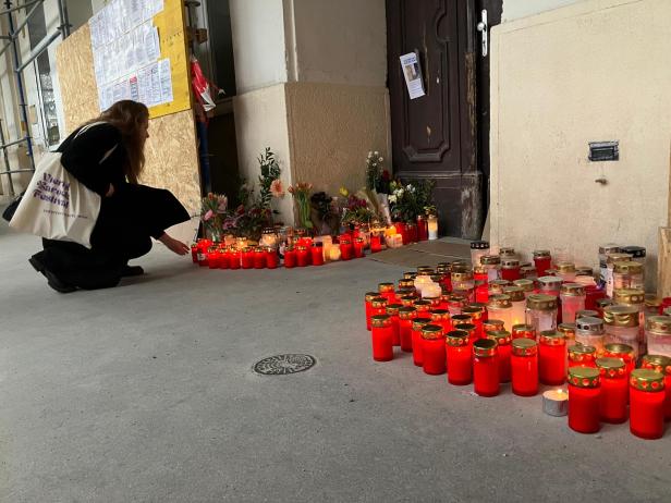 Eine Frau kniet vor zahlreichen Kerzen und Blumen, die am Eingang eines Gebäudes in der Porzellangasse zum Gedenken an die verstorbenen Bauarbeiter aufgestellt wurden.