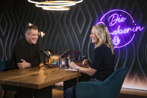 Armin Assinger und Monika Gruber sitzen einander gegenüber und sprechen miteinander