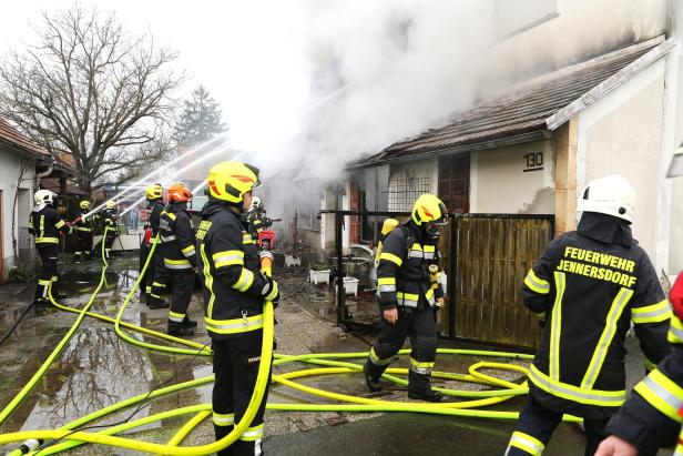 Mehrere Feuerwehrleute bekämpfen mit Wasserschläuchen einen Brand in einem stark qualmenden Wohnhaus.