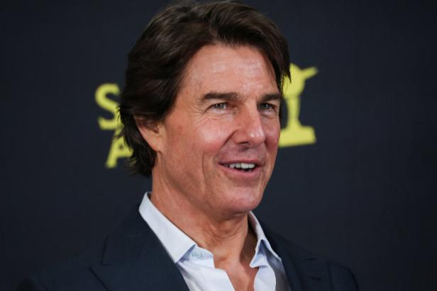 Tom Cruise lächelt vor einem dunklen Hintergrund mit gelber Schrift.