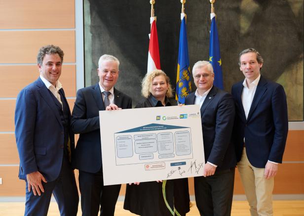 Vier Männer im Anzug und eine Frau halten ein Schild, das über die künftige Versorgung in Gmünd informiert.