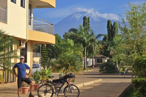 Mann mit Fahrrad und drei Kindern am weißen Sandstrand vor türkisblauem Meer und Segelbooten.
