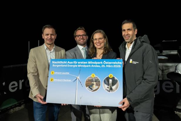 Vier Personen halten ein Schild mit Informationen zum Windpark Andau und dem Nachtlicht-Aus am 25. März 2026.