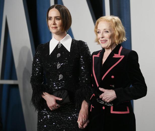 Sarah Paulson und Holland Taylor stehen nebeneinander und halten Händchen vor einem Vanity Fair Hintergrund.
