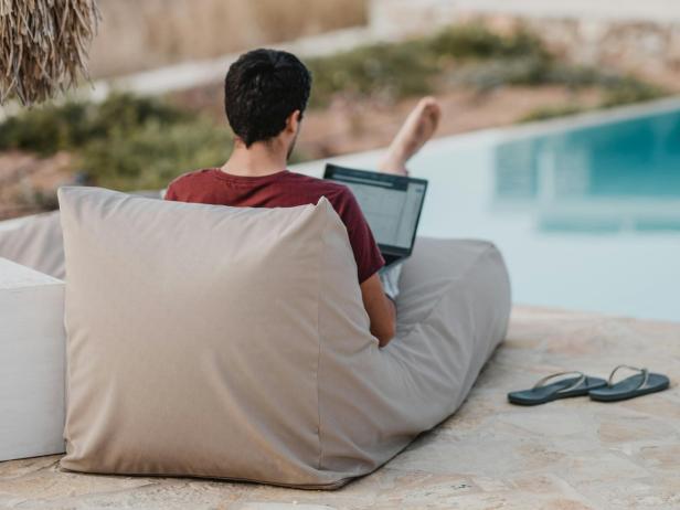 Eine Person arbeitet entspannt mit einem Laptop auf einem Sitzsack am Pool und symbolisiert die ortsunabhängige Flexibilität des Fernstudiums.