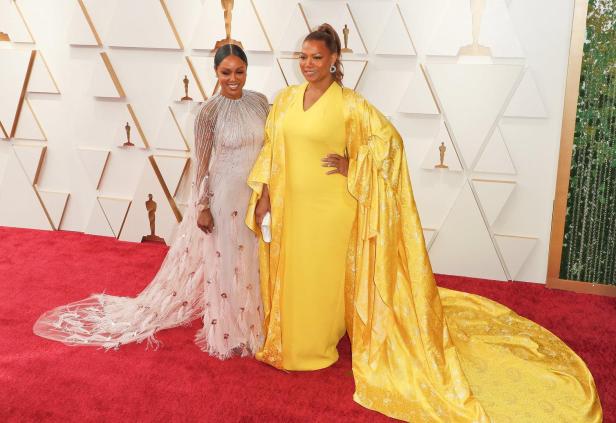 Zwei Stars in eleganten Kleidern posieren gemeinsam auf dem roten Teppich einer Preisverleihung und setzen ein Zeichen für queere Sichtbarkeit.