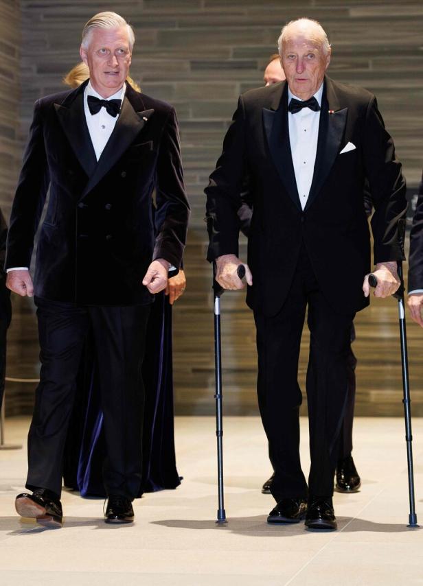 König Philippe und König Harald in schwarzen Smokings gehen nebeneinander, Harald benutzt zwei Gehhilfen.