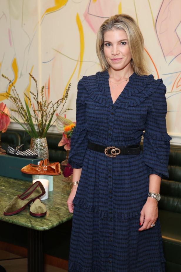 Natasha Archer steht in einem eleganten blauen Kleid an einem Tisch mit Schuhen und Blumen, passend zu ihrem Neustart als Creative Consultant.