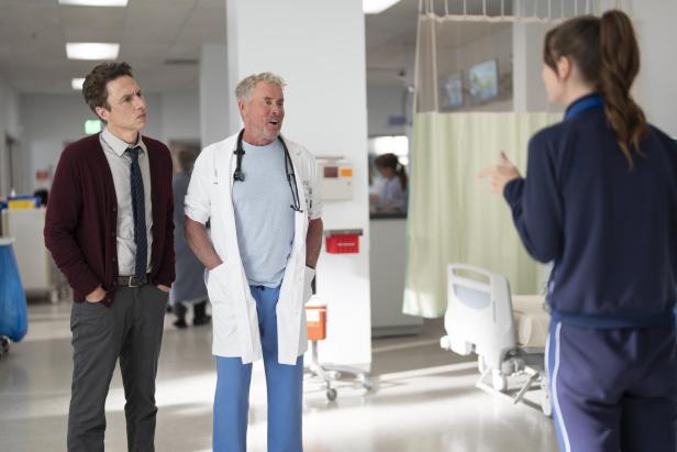 Zwei Männer, einer im Arztkittel, sprechen mit einer Frau in Sportkleidung auf einem Krankenhausflur.