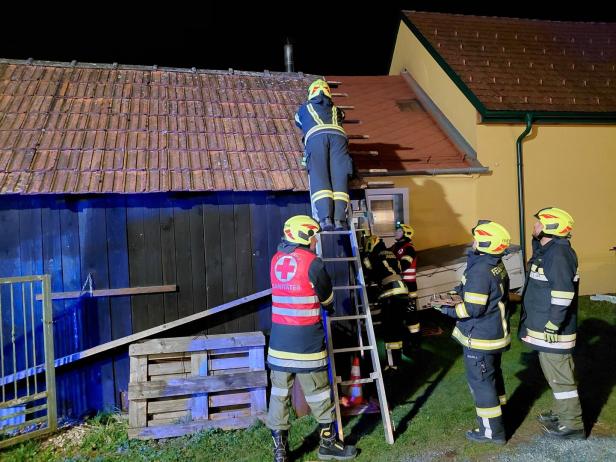 Mehrere Feuerwehrleute und ein Sanitäter arbeiten nachts mit einer Leiter an einem Hausdach.