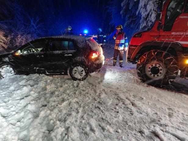 Ein Auto steckt im Schnee fest, Feuerwehrleute und ein Einsatzfahrzeug helfen bei winterlichen Bedingungen.