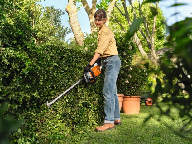 Eine Frau schneidet mit einer STIHL Akku-Heckenschere eine Hecke im Garten und demonstriert die einfache Handhabung moderner Gartengeräte.
