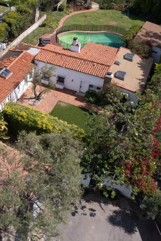 Haus mit rotem Ziegeldach, Garten, Bäumen und umzäuntem Swimmingpool im Hinterhof.