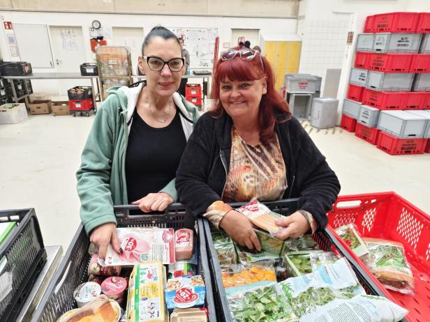 Zwei Frauen stehen lächelnd hinter Kisten voller Lebensmittel.