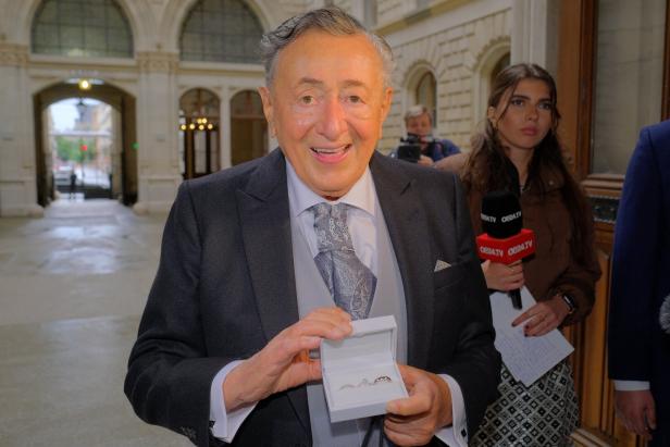 Ein Mann im Anzug präsentiert Eheringe in einer Schatulle vor Reportern.