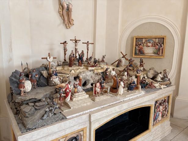 Mehrere Figuren stellen die Kreuzigung Jesu und Szenen seines Leidenswegs auf einem steinernen Podest mit Kreuzen und römischen Soldaten dar.