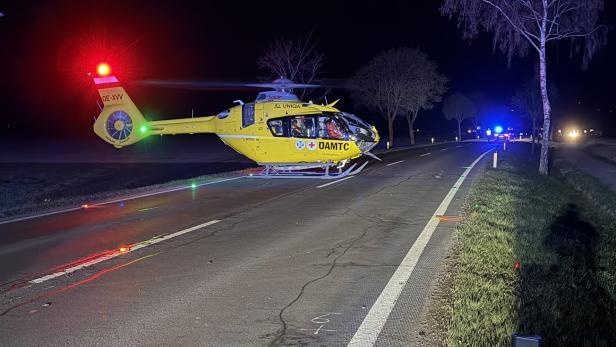 Ein gelber Rettungshubschrauber steht nachts auf einer Landstraße, Blaulichter von Einsatzfahrzeugen im Hintergrund.