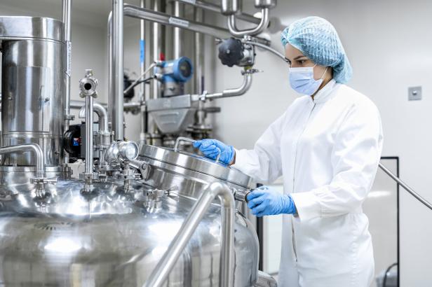 Eine Person in Schutzkleidung arbeitet an einem großen Edelstahltank in einer sterilen Produktionsumgebung.