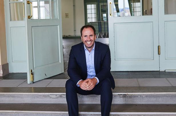 Christoph Pieh sitzt auf den Stufen vor einer offenen Tür und lächelt in die Kamera