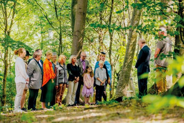 Menschen stehen im Wald in einer Trauerzeremonie um eine Urne versammelt.