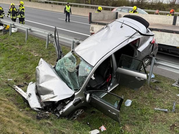 Ein silbernes Auto mit stark beschädigter Front steht neben der Leitplanke, umgeben von Feuerwehrleuten und Polizei.