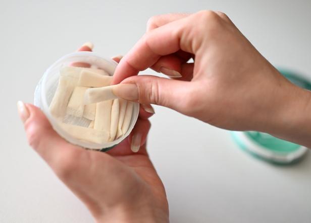 Eine Hand hält eine Dose mit mehreren weißen Nikotinbeuteln, während die andere Hand einen Beutel entnimmt.