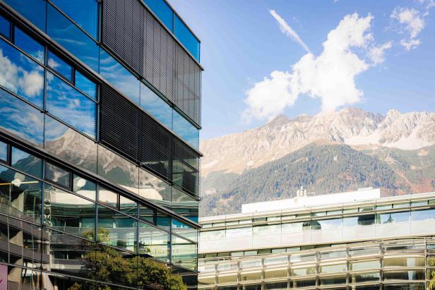 Moderne Glasfassaden des MCI-Campus in Innsbruck mit Blick auf die umliegenden Alpen bei klarem Himmel.