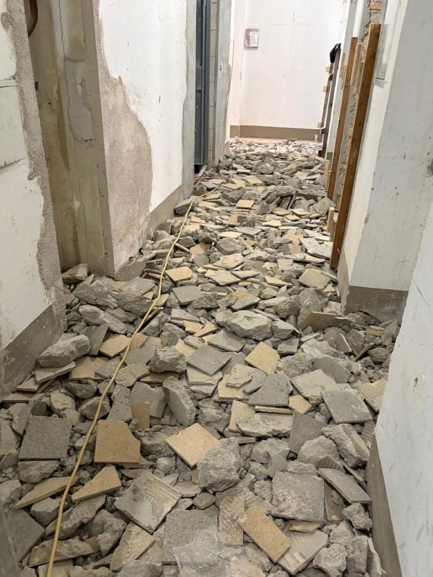 Ein Flur voller zerbrochener Fliesen und Bauschutt, die den gesamten Boden bedecken.