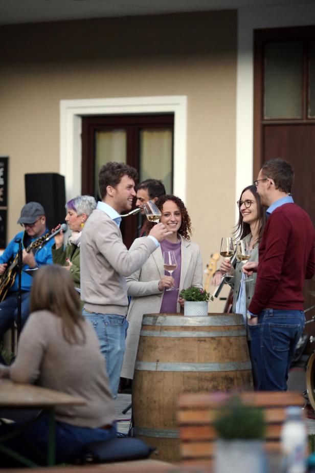 Menschen stehen vor Weinfass bei Winzer im Hof und verkosten Wein.