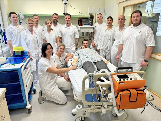 Eine Gruppe von medizinischem Personal steht um ein Krankenbett mit einer Übungspuppe und medizinischen Geräten.