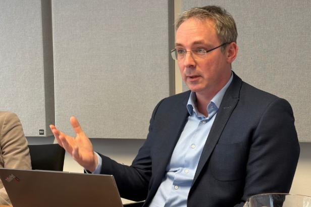 Ein Mann im Anzug spricht gestikulierend in einem modernen Büro mit Laptop vor sich.