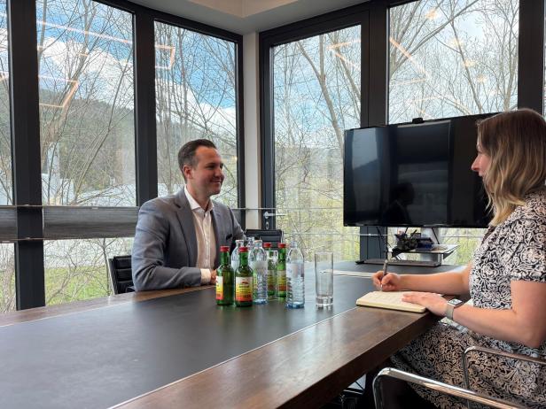 Zwei Personen sitzen an einem Konferenztisch, unterhalten sich und vor ihnen stehen mehrere Getränke.