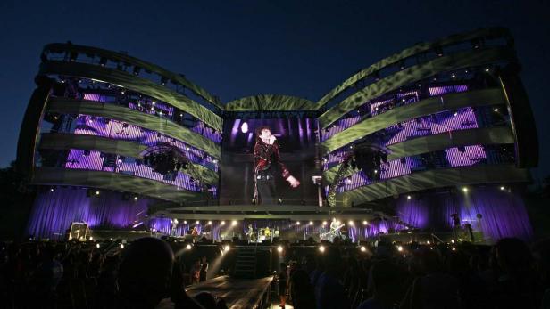 Mick Jagger tritt auf einer großen Bühne mit lila Lichtern vor einem Publikum auf.