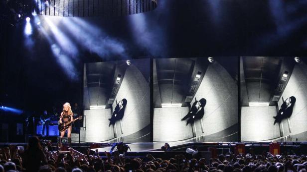 Madonna spielt Gitarre auf einer Bühne vor einer großen Menschenmenge.