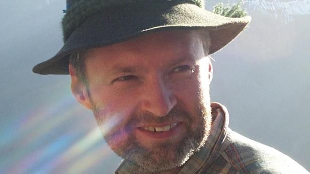 Mann mit Bart und kariertem Hemd trägt einen traditionellen Hut, Sonnenstrahlen fallen schräg über sein Gesicht.