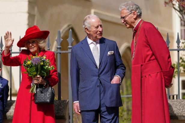 König Charles spricht mit einem Bischof, während Camilla winkt und einen Blumenstrauß hält.