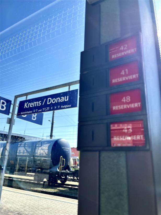 Ein Bahngleis mit einem Schild „Krems / Donau“, einem Güterwaggon und mehreren reservierten Sitzplatzanzeigen.