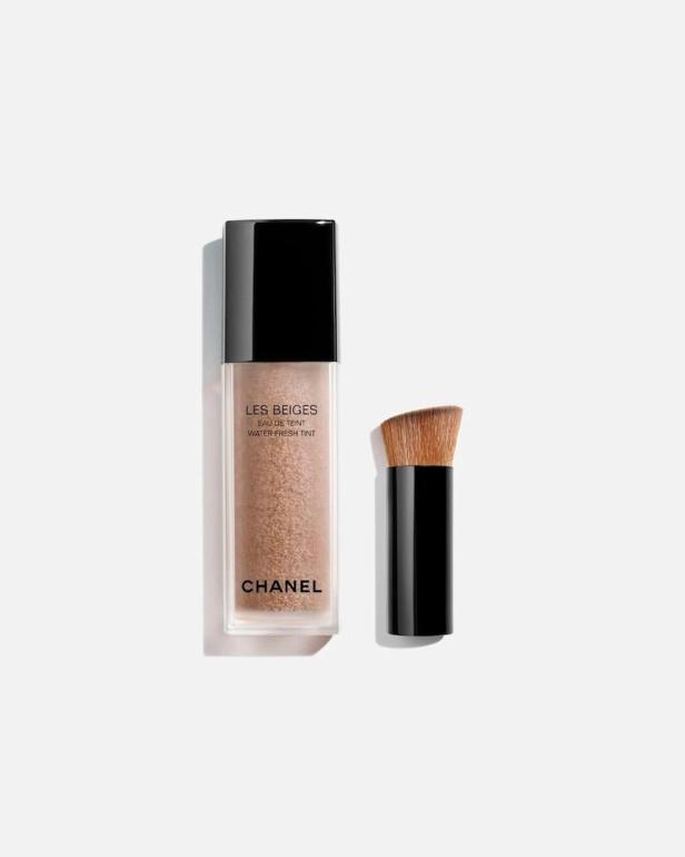 Ein transparenter Flakon mit beigem Make-up und schwarzem Deckel steht neben einem kurzen Pinsel mit braunen Borsten.