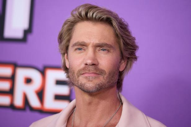 Chad Michael Murray lächelt vor lila Hintergrund.