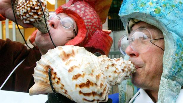 Zwei Personen in Kostümen und übergroßen Brillen blasen in Muscheln.