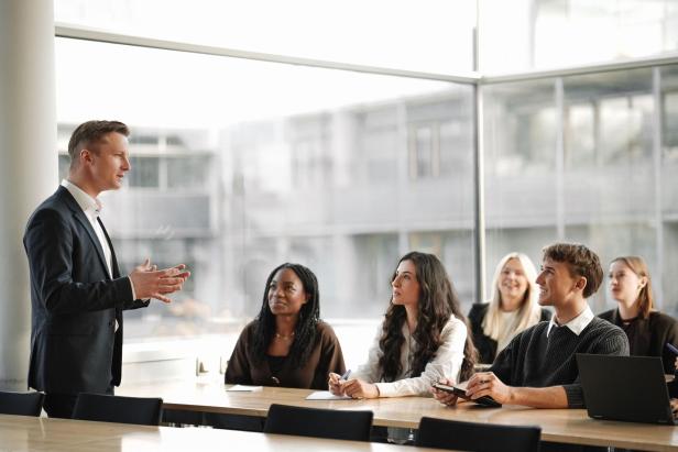 Ein Dozent aus der Wirtschaft spricht vor einer Gruppe aufmerksamer Studierender im modernen Hörsaal des MCI Innsbruck.