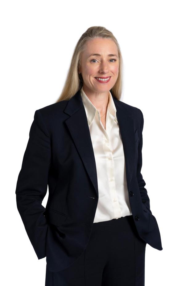 Eine Frau mit blonden Haaren lächelt in einem dunklen Blazer und einer hellen Bluse.